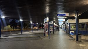 Estación de autobuses de Sarajevo de noche, con andenes vacíos y luces frías reflejadas en el pavimento.